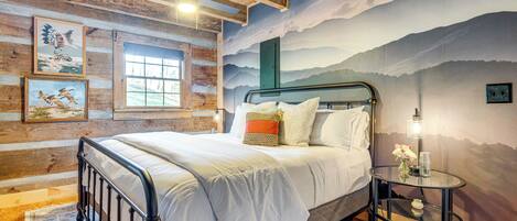 Un dormitorio con cama, una mesa redonda de vidrio, un ventilador de techo y un mural de montañas.
