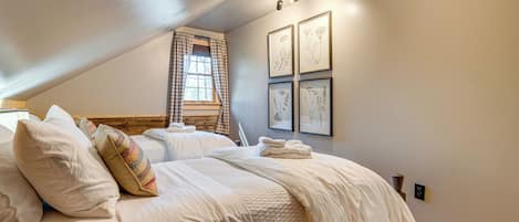 A bedroom with two beds, a window with curtains, and framed botanical prints on the wall.