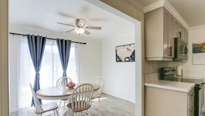Zona pranzo con tavolo rotondo, sedie bianche e ventilatore a soffitto.