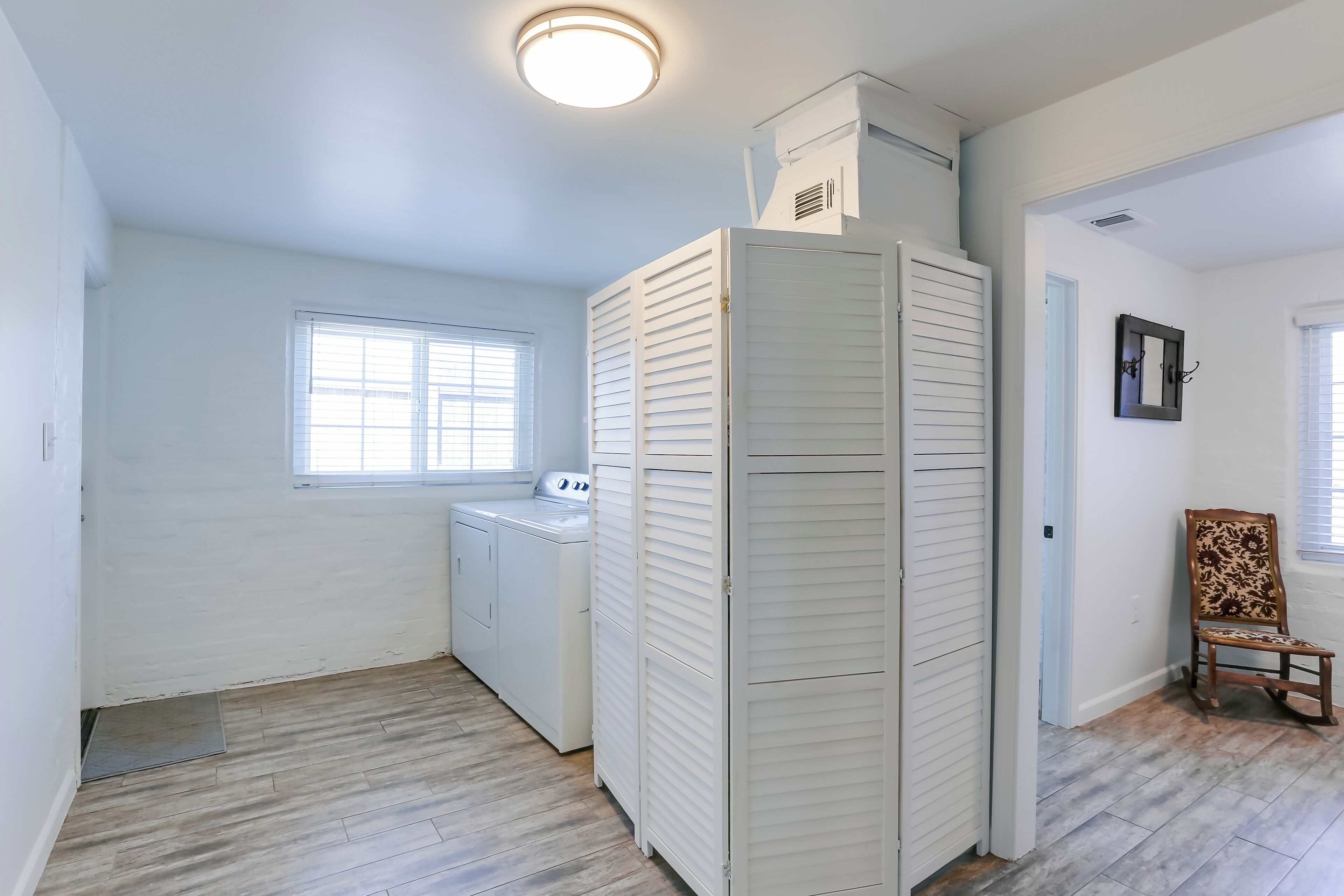 A laundry room with a washing machine, a tall white closet, and a chair.