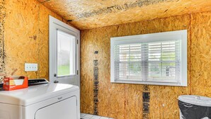 A room with a wooden wall, a window with blinds, a washing machine, and a trash can. - Peaceful Home w/ Patio on 30 Acres in Coxs Creek! (Coxs Creek)