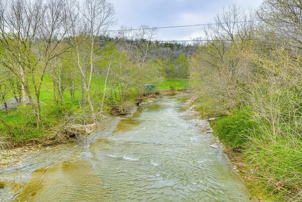 A river flowing through a forested area with a small structure in the distance. - Peaceful Home w/ Patio on 30 Acres in Coxs Creek! (Coxs Creek)