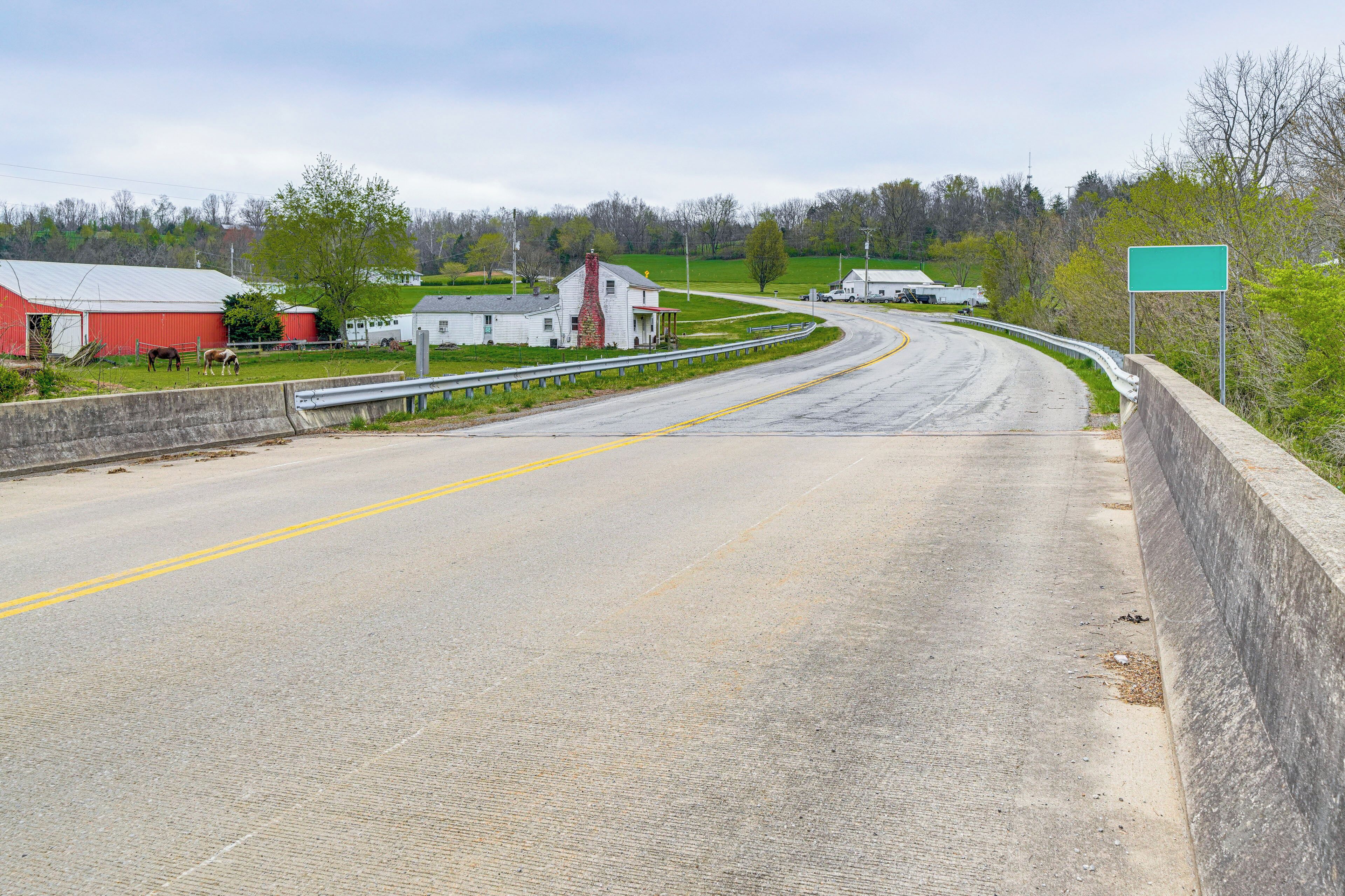 A rural road with a barn and a white house.