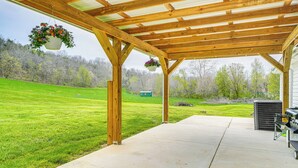 A covered patio with a concrete floor, wooden beams, and hanging flower baskets. - Peaceful Home w/ Patio on 30 Acres in Coxs Creek! (Coxs Creek)