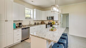 Una cocina moderna con armarios blancos, encimera de granito y una isla central con taburetes.