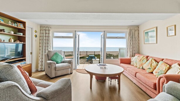 A living room with a sofa, armchairs, a coffee table, and a television. There is a large window with a view of the sea. - The Coastal Crab - Family-friendly Three-bed Beach House in Pevensey (Pevensey)