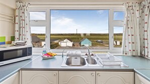 A kitchen with a large window, a sink, a microwave, and a dish rack. - The Coastal Crab - Family-friendly Three-bed Beach House in Pevensey (Pevensey)