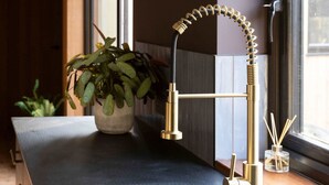 A kitchen with a black sink, a gold faucet, and a potted plant on the counter. - Modern 2-bed Cabin Near West Wittering Beach (Chichester)
