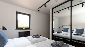 A modern hotel room with two beds, a large mirror, and a window providing natural light. - Modern 2-bed Cabin Near West Wittering Beach (Chichester)