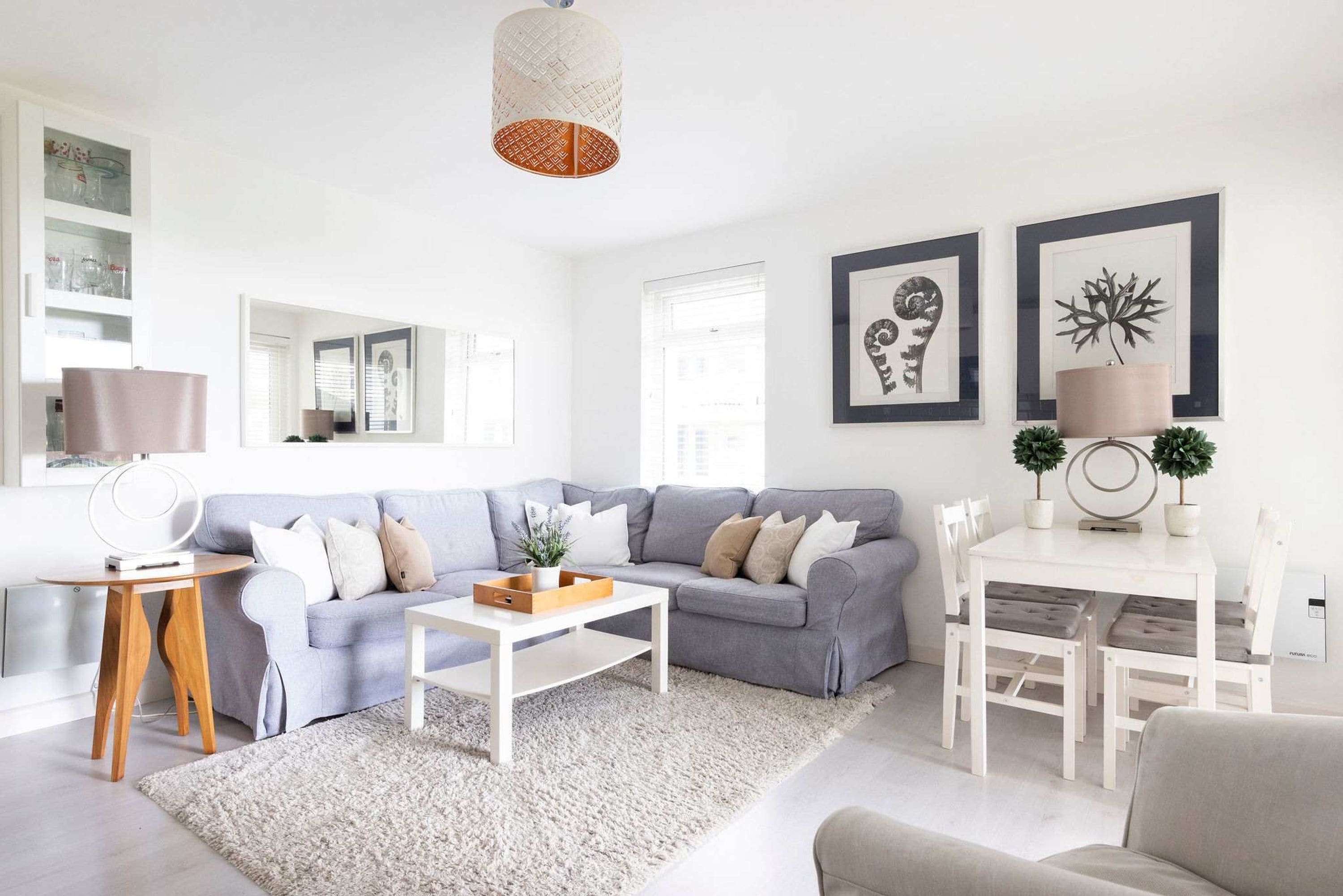 Una sala de estar moderna con un sofá gris, una mesita de centro blanca y un comedor con una mesa y sillas blancas.