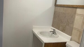 Een kleine, compacte badkamer met een witte wastafel, een spiegel erboven en een toilet.