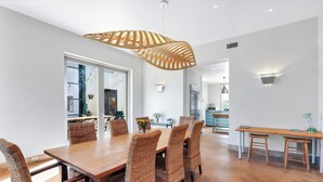 A dining area with a wooden table and wicker chairs, a hanging light fixture, and a view into the kitchen. - The Plant at Kyle I Pool, Architectural Landmark (Kyle)