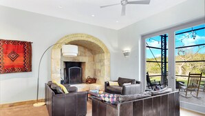 A modern living room with leather sofas, a stone fireplace, and a large sliding glass door leading to an outdoor patio. - The Plant at Kyle I Pool, Architectural Landmark (Kyle)