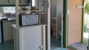 A compact kitchen with a microwave, shelves, and a window.