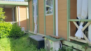 A mobile home with a green exterior, large windows, and a small porch area.