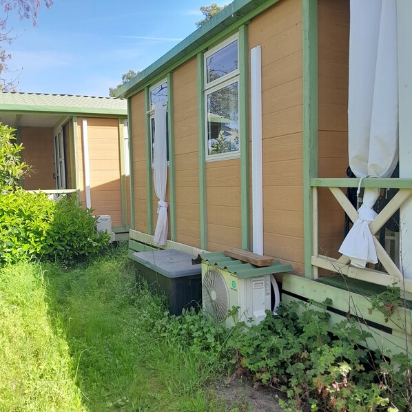 A mobile home with a green exterior, large windows, and a small porch area.