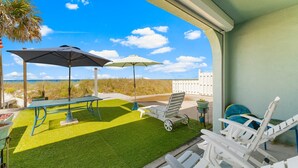 Eine Terrasse mit Tisch, zwei Sonnenschirmen und Liegestühlen mit Blick auf einen Strand.