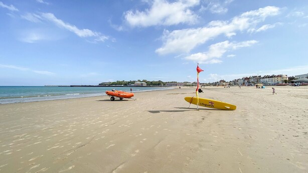 Una playa con equipo de salvavidas, incluyendo una tabla de surf amarilla y un bote inflable naranja.