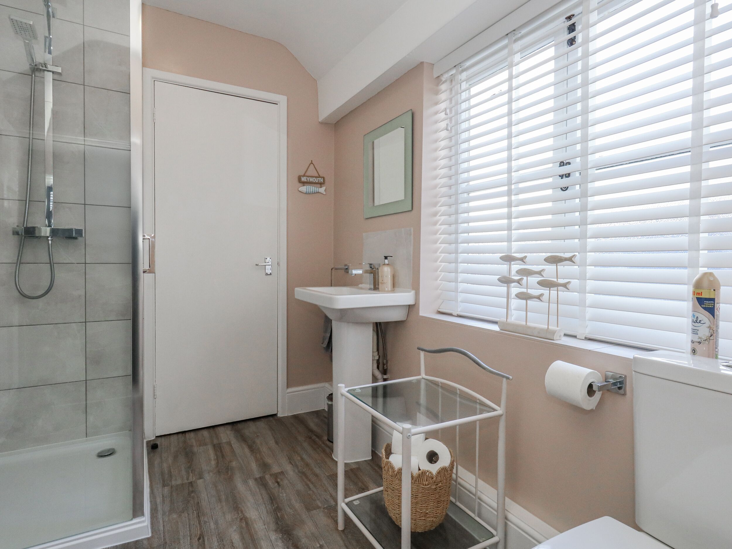 Ein Badezimmer mit Dusche, Waschbecken, Toilette und einem Fenster mit Jalousien.