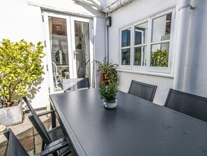 A patio with a table and chairs, a potted plant, and a view of a building with windows and a door.