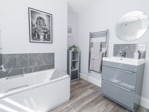 A modern bathroom with a bathtub, a vanity with a mirror, and a framed picture on the wall.