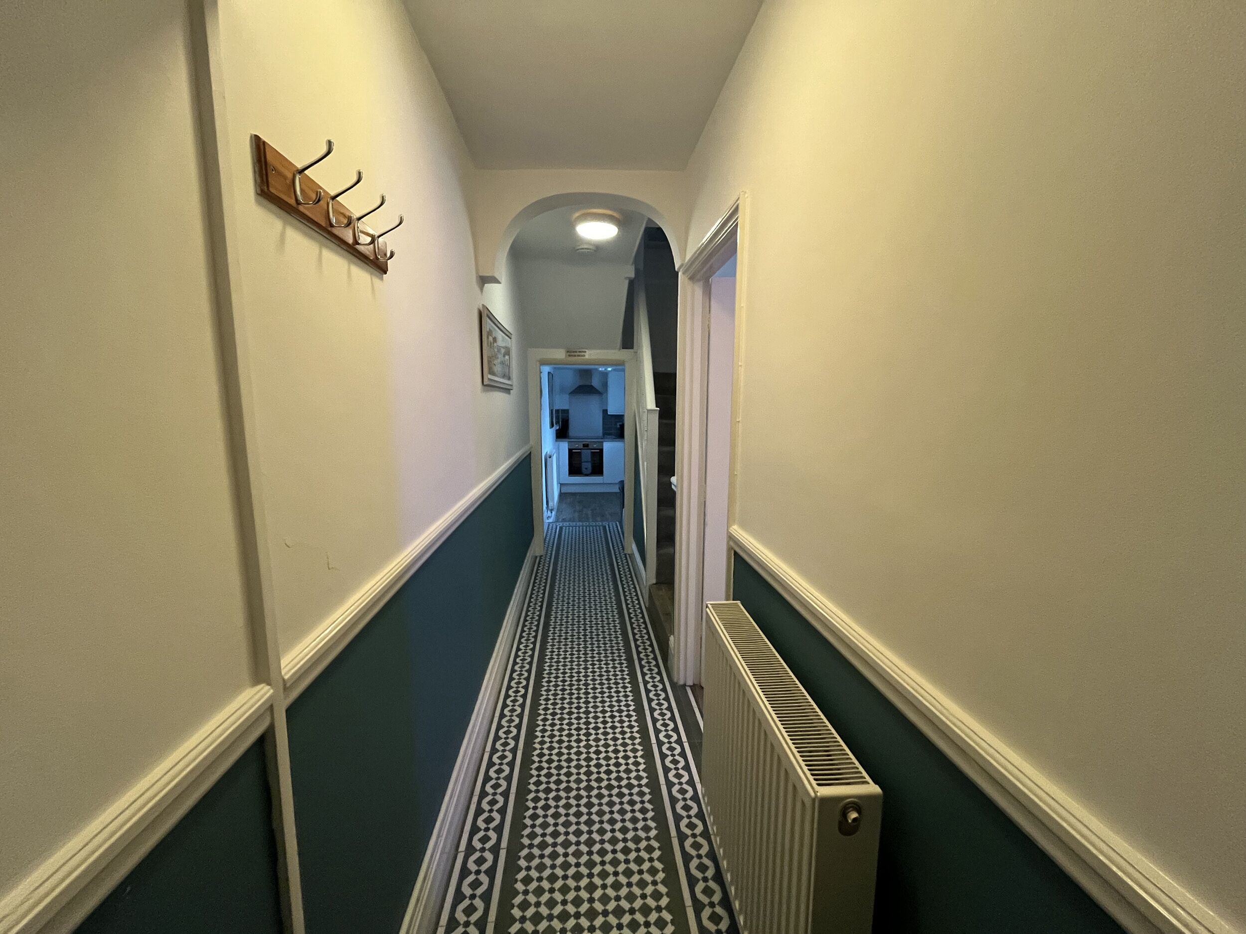 Un couloir étroit avec un sol à motifs, un porte-manteau et un radiateur.