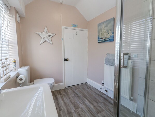A bathroom with a white toilet, a shower area, a star decoration, and a painting of a sailboat. - Shrimp Cottage (Weymouth)