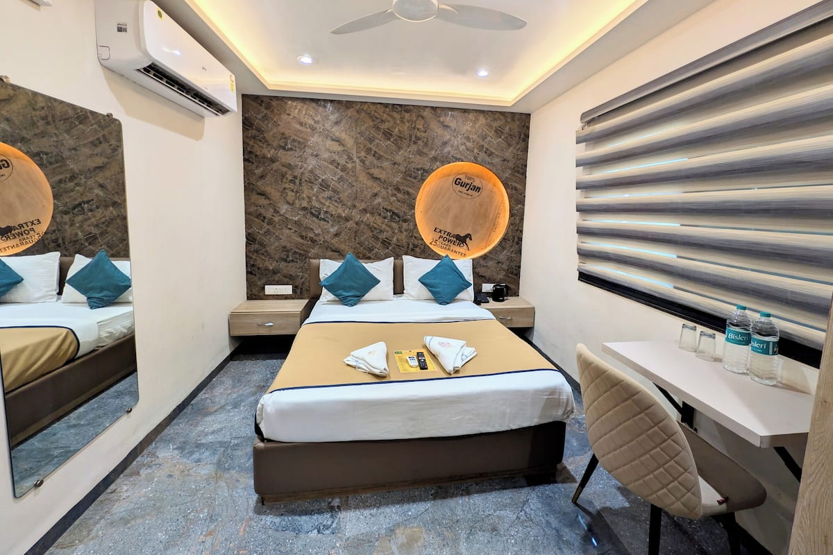 A hotel room with a bed, bedside tables, a desk, a chair, an air conditioning unit, a ceiling fan, and a wall with a textured pattern.