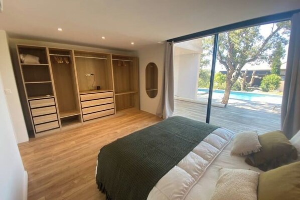 A bedroom with a large bed, a walk-in closet, and a view of a swimming pool.