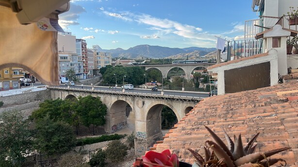 Vista di un ponte in pietra con archi, una strada con veicoli e edifici sullo sfondo.