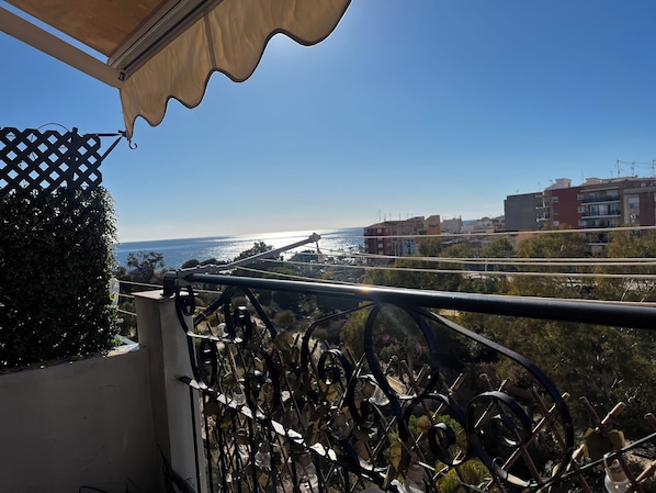 Ein Balkon mit Meerblick, einem Metallgeländer und Gebäuden im Hintergrund.