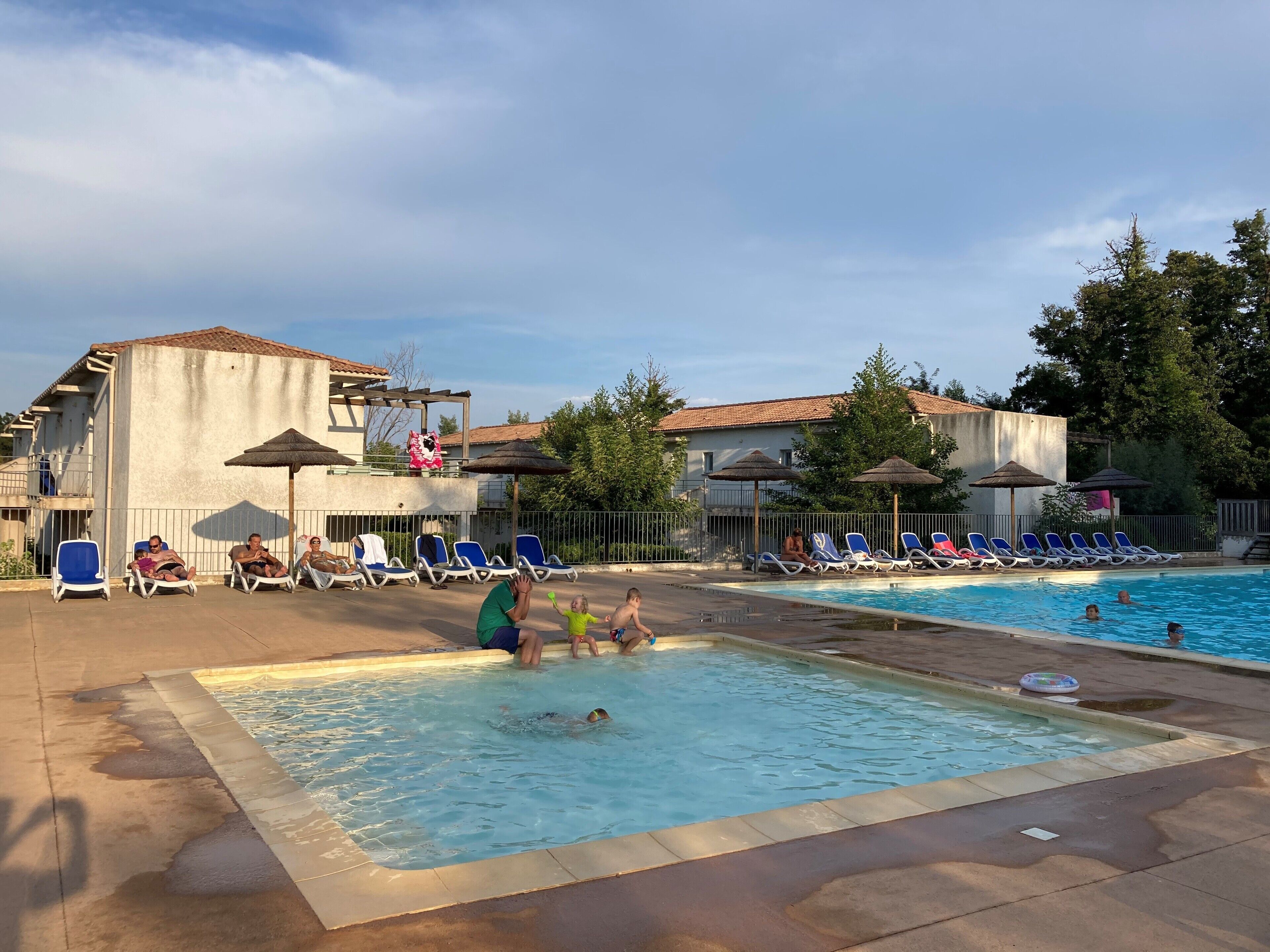 Ein Poolbereich mit Liegestühlen und Sonnenschirmen, umgeben von Gebäuden mit einem Ziegeldach.