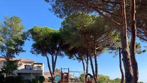 A playground with climbing structures and a slide, surrounded by trees and a building with a red-tiled roof. - Apartment with terrace and direct access to pool & beach (Poggio-Mezzana)