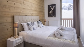 A bedroom with a wooden wall, a bed with white bedding, a mounted deer picture, and a window with curtains. - Apartment in La Rosiere With Alpine Views (Montvalezan)