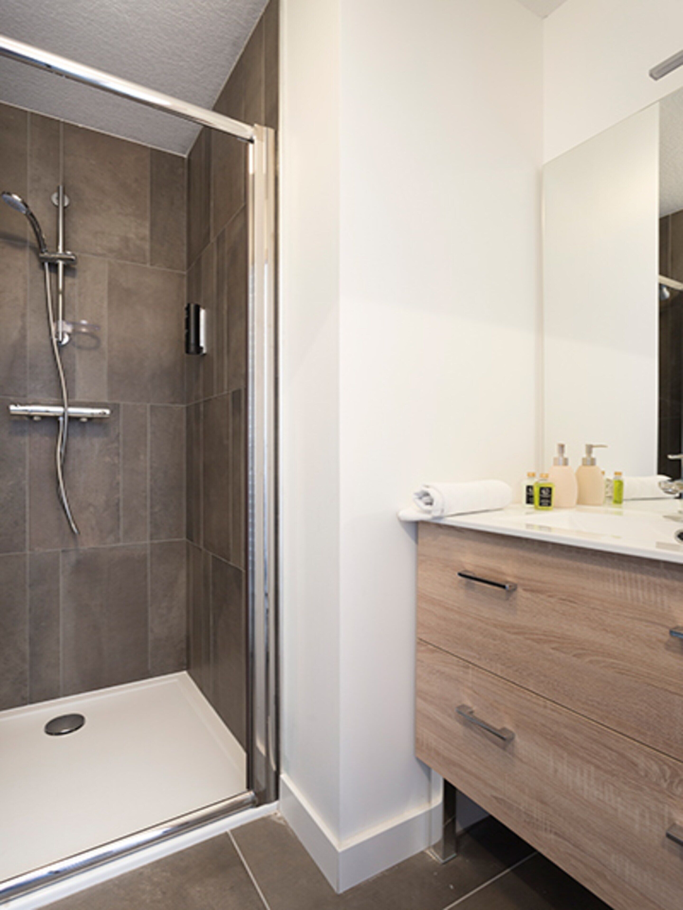 A modern bathroom with a shower, a vanity with a mirror, and toiletries.