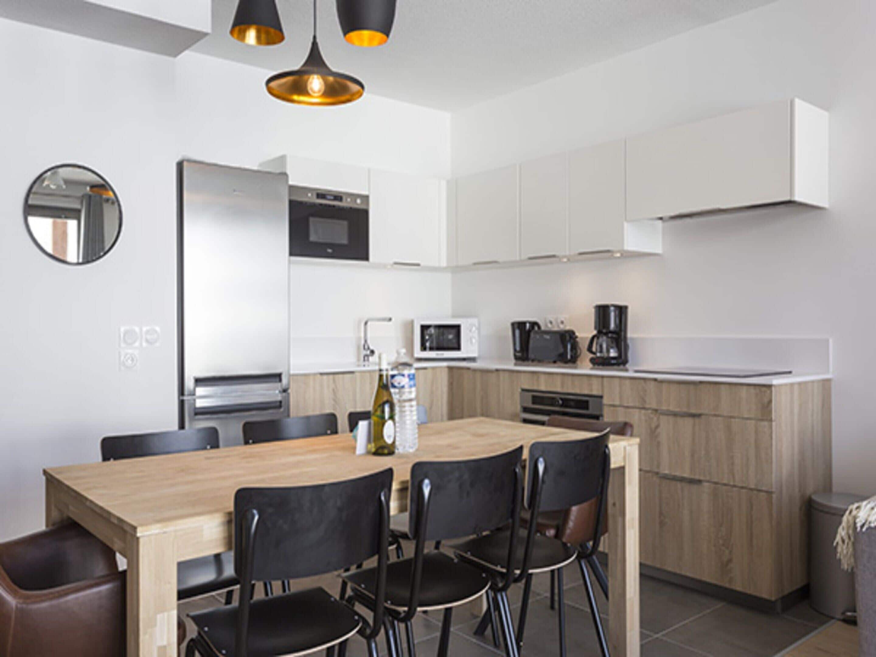 A modern kitchen with white cabinets, a wooden dining table, and black chairs.