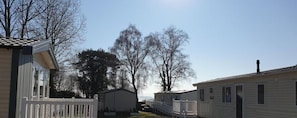 Een rijstaande vakantiewoningen met een omheinde tuin, bomen en een heldere lucht.