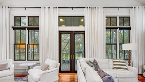 A spacious living room with white furniture, large windows, and a view of the outdoors.