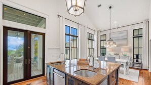 A modern kitchen with a large island, double sinks, and a dining area with a table and chairs.
