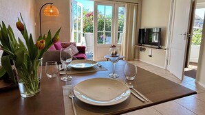 Un comedor con una mesa dispuesta para dos personas, un jarrón de tulipanes y un televisor al fondo.