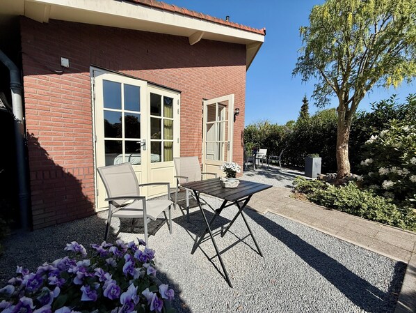A brick building with a patio area featuring a table and chairs, surrounded by gravel and potted plants.