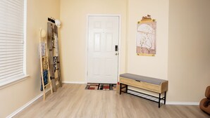 Un couloir avec une porte blanche, un banc, une petite table et un tableau accroché au mur.