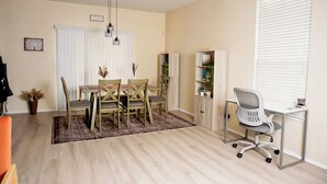 Un salon moderne comprenant un coin repas, un espace de travail et une fenêtre équipée de stores.