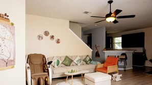 Un salon comprenant un canapé, des fauteuils, un fauteuil massant, une petite table et un ventilateur de plafond.