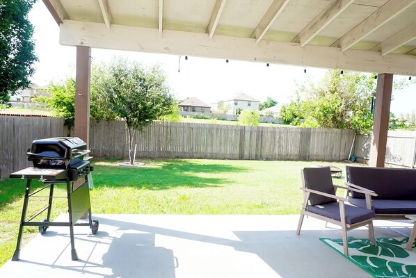 Un patio cubierto con una parrilla, sillas y un jardín con césped.