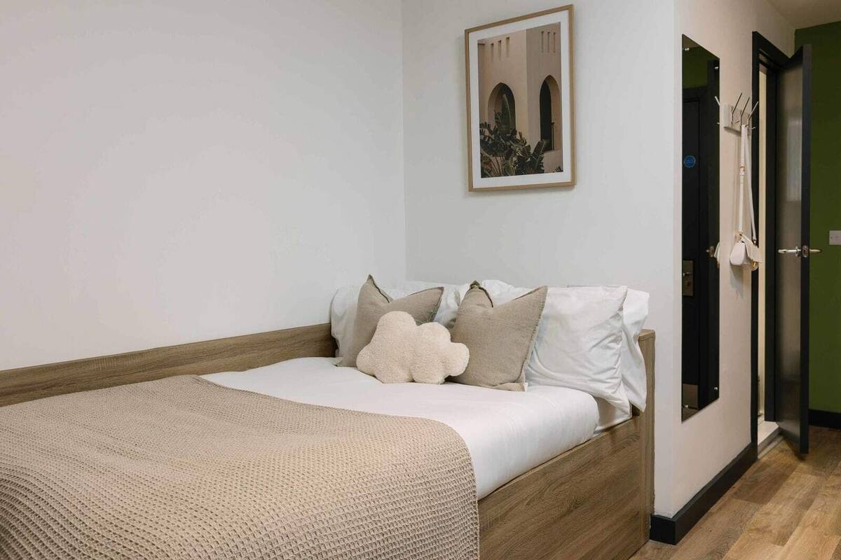 Une chambre à coucher avec un lit, des oreillers, une couverture et un tableau encadré accroché au mur.