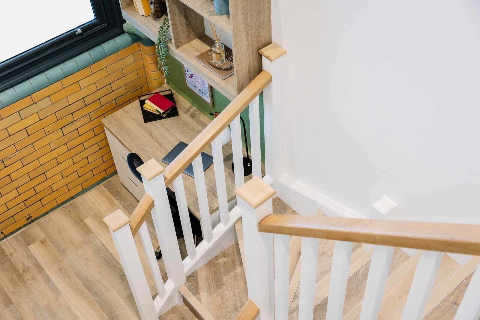 A staircase with white railings and wooden steps leading to a landing with a small table and a chair.