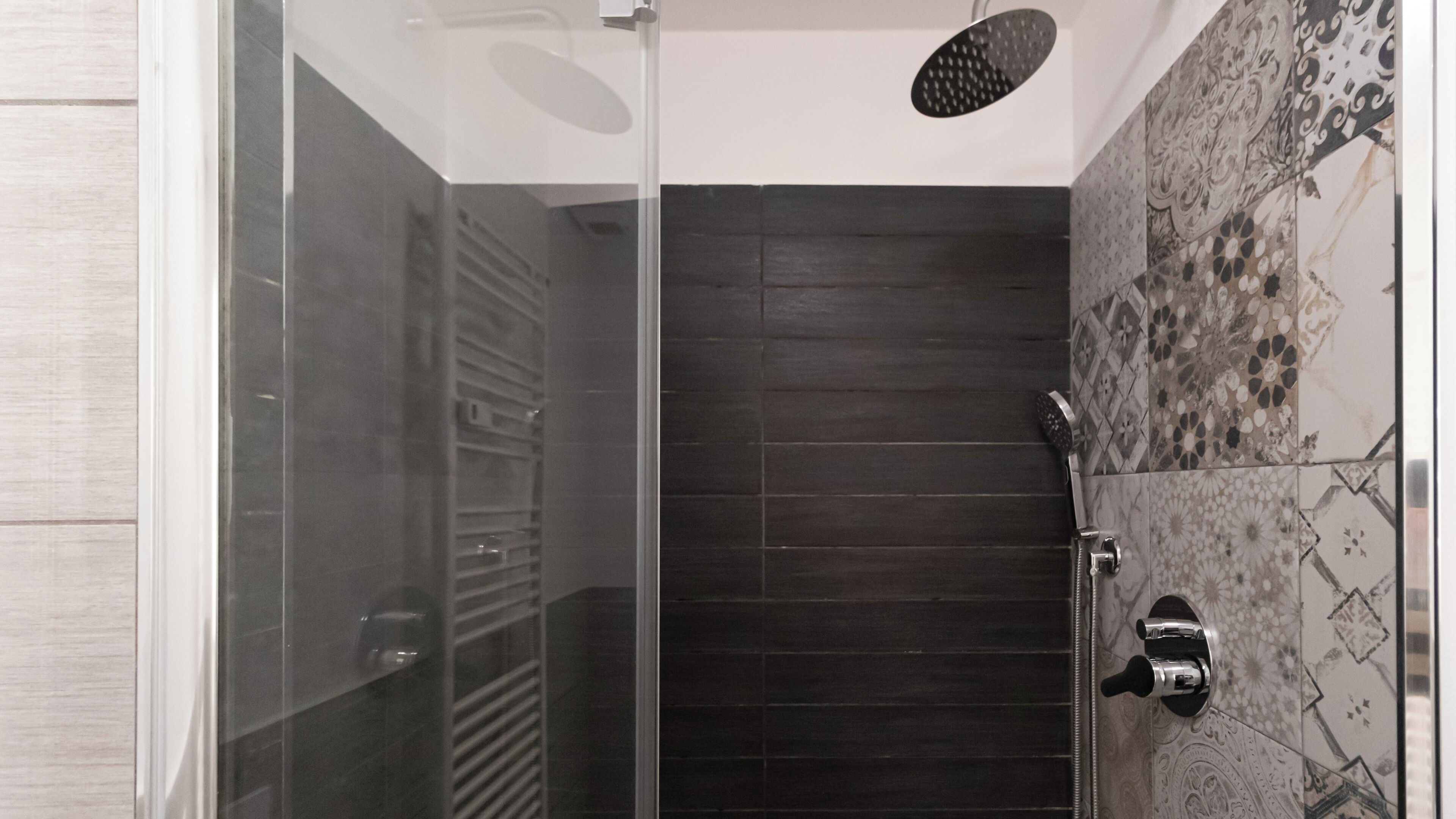 A modern shower with a glass enclosure, dark tiles, and a patterned tile wall.