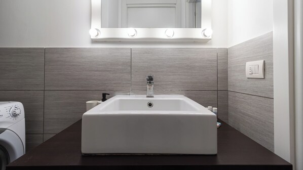 A bathroom with a white sink, a mirror with lights, and a washing machine.