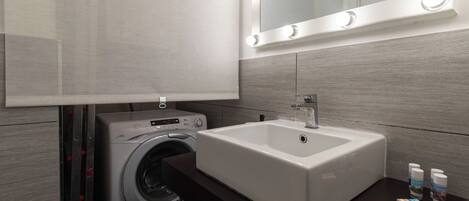 A modern bathroom with a built-in washing machine, a sink with a mirror above, and toiletries on the counter.